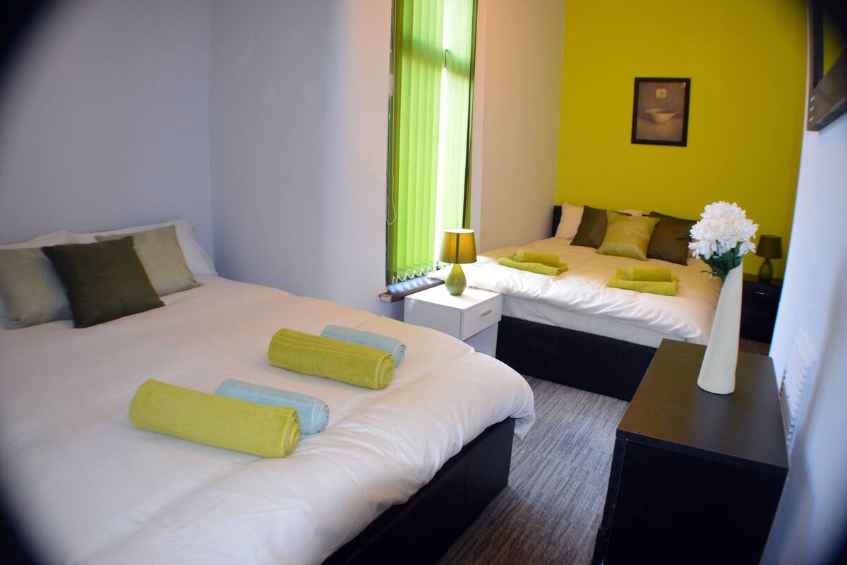 A hotel room with two beds, each with neatly folded towels, a bedside table with a lamp, and a vase with flowers.