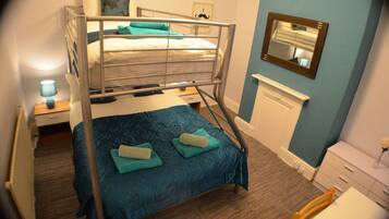 A bunk bed room with a blue bedspread, a nightstand with a lamp, a dresser, and a mirror on the wall.