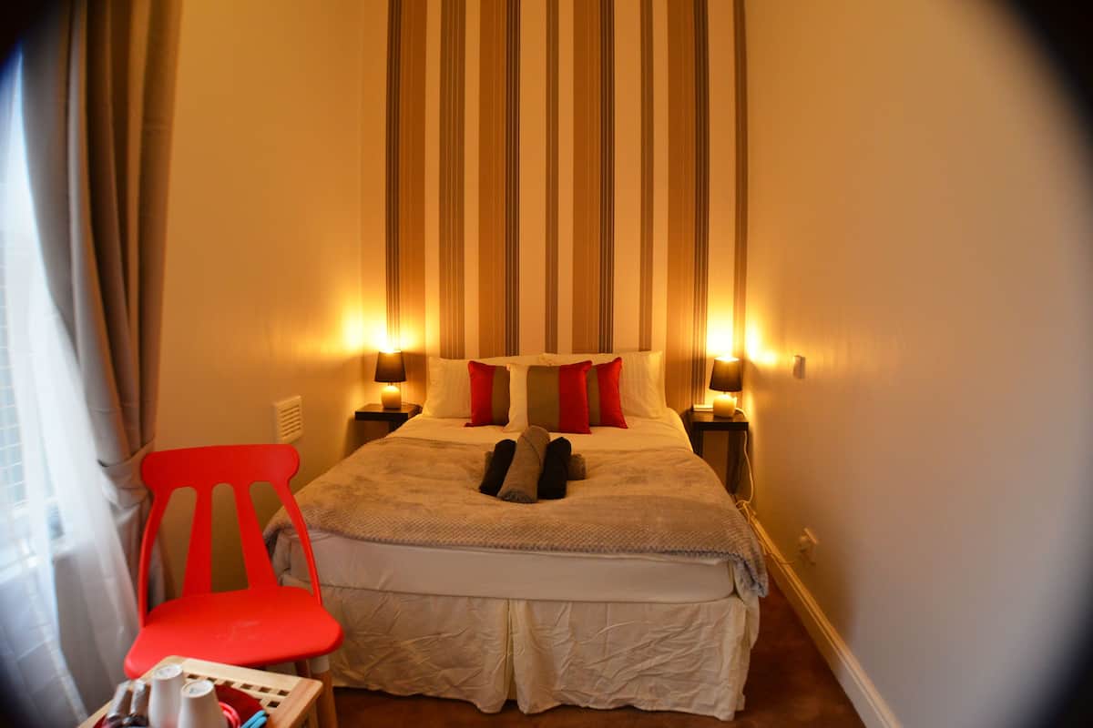 A hotel room with a bed, a red chair, and two bedside lamps.