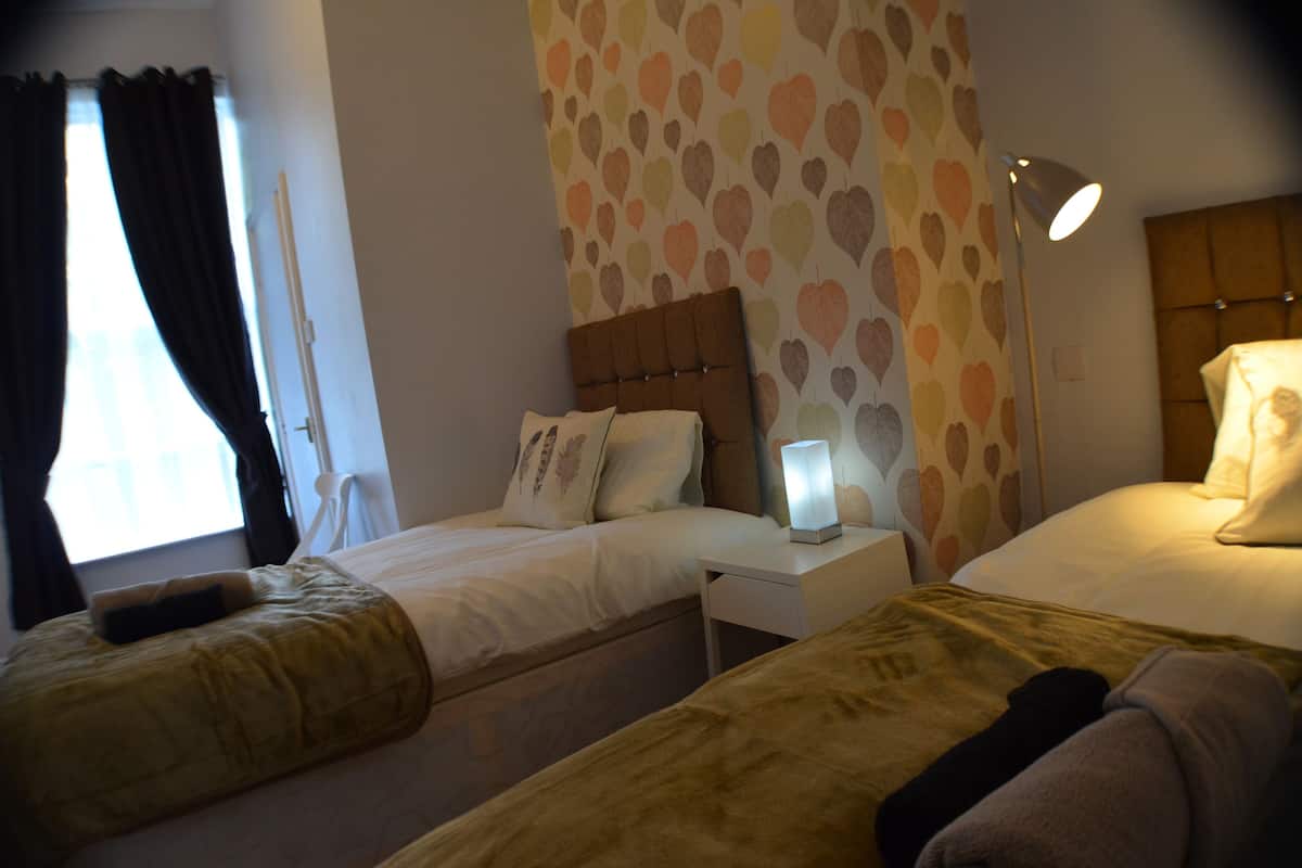 A hotel room with two beds, a bedside table with a lamp, and a wall with a heart pattern.