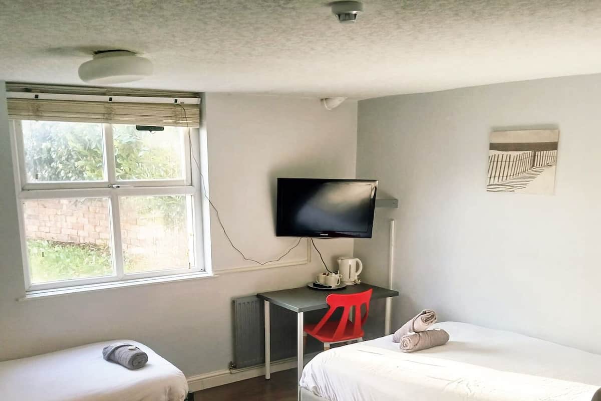 A room with two single beds, a desk with a TV, and a window with blinds.