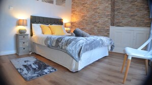Una camera da letto con un letto, comodini, una poltrona, un tappeto e un muro in pietra.