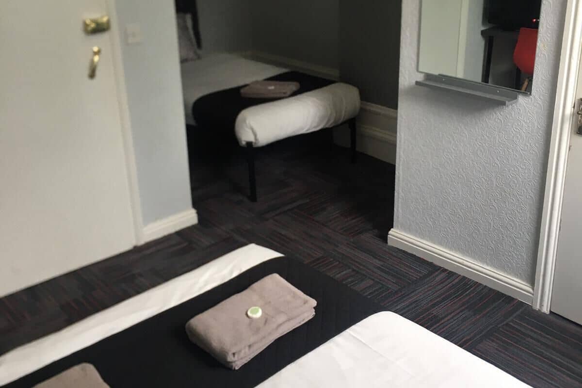 A hotel room with a bed, a bench, a small table, and a mirror.