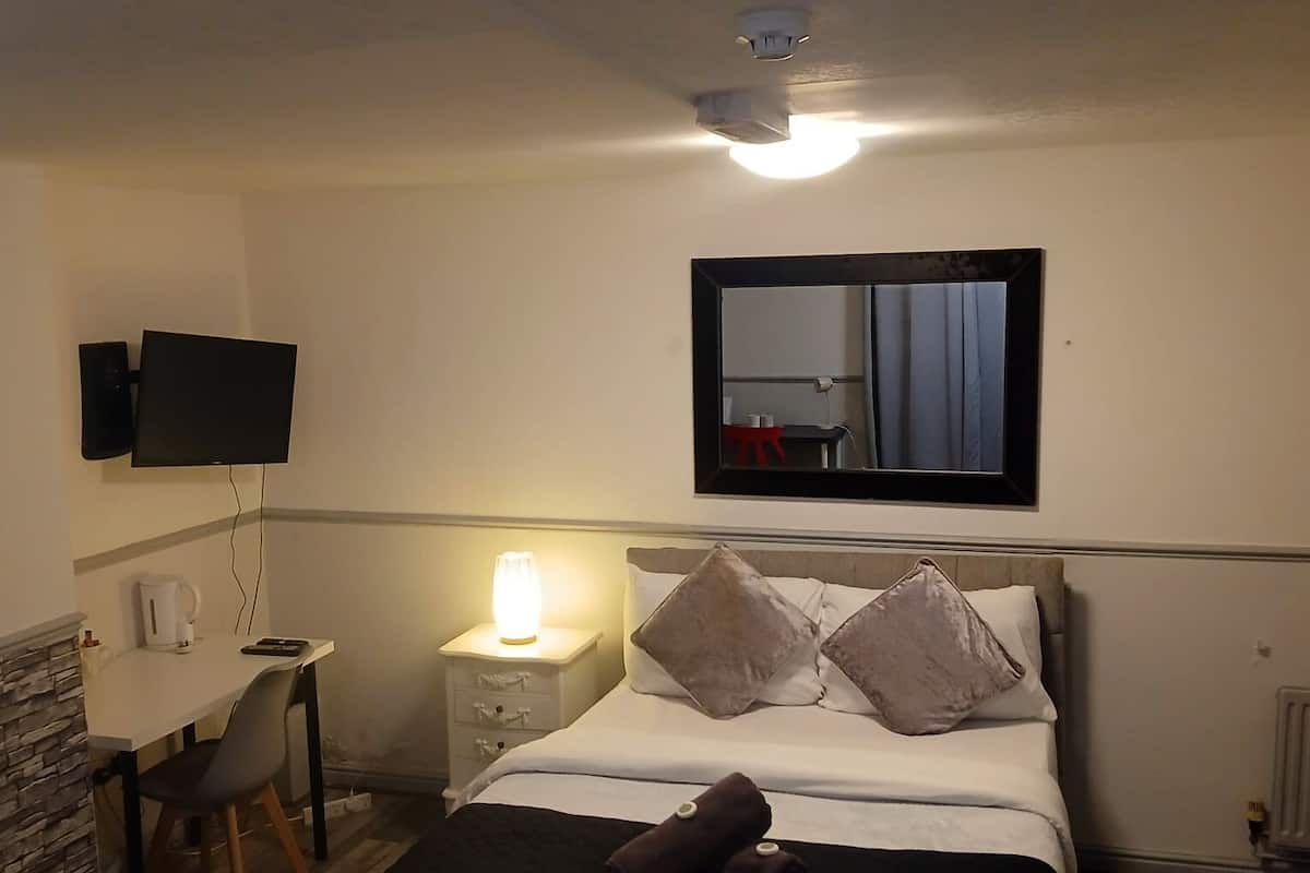 A hotel room with a bed, bedside table, lamp, TV, and a small desk with a chair.