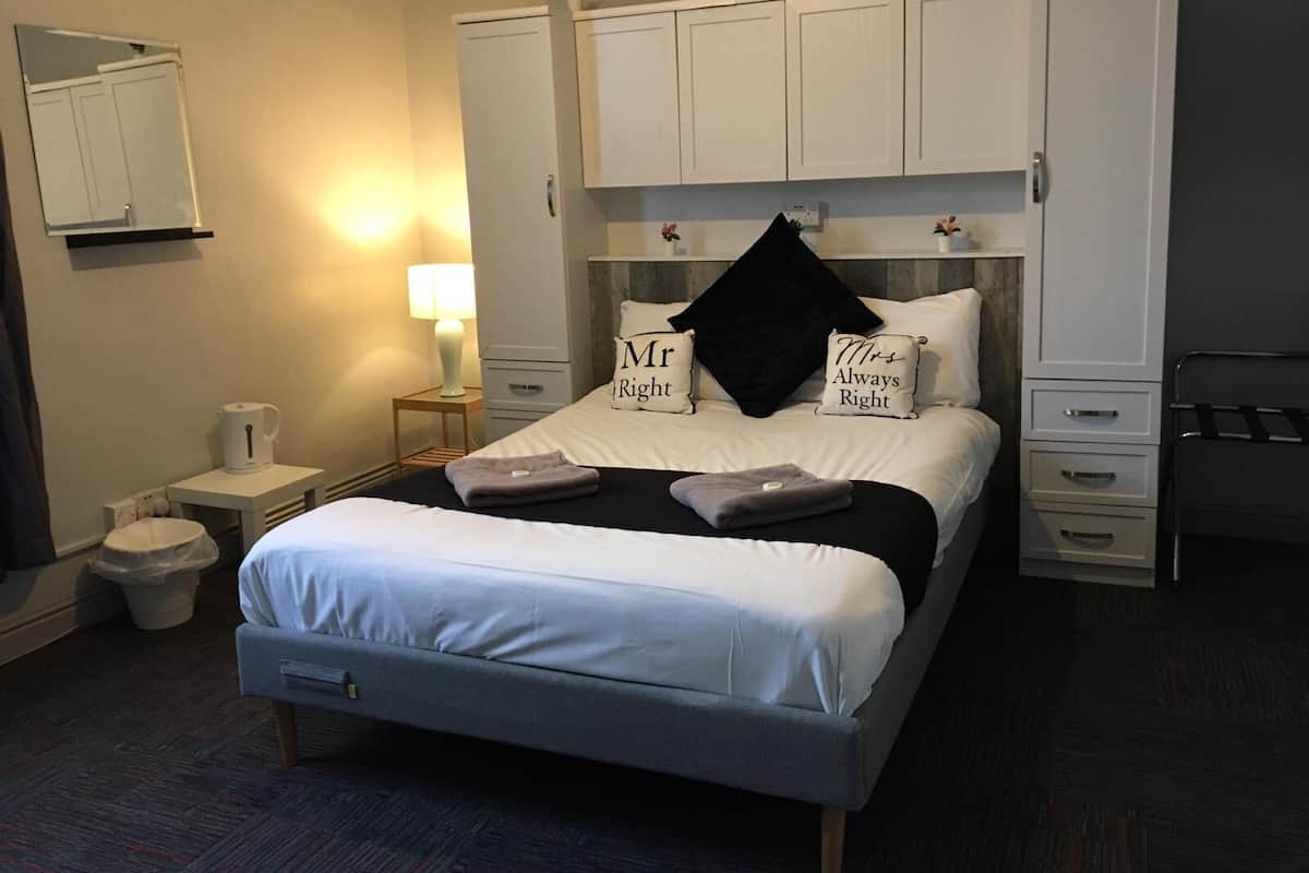 A neatly arranged hotel room with a bed, bedside tables, a lamp, a wardrobe, and a small trash bin.