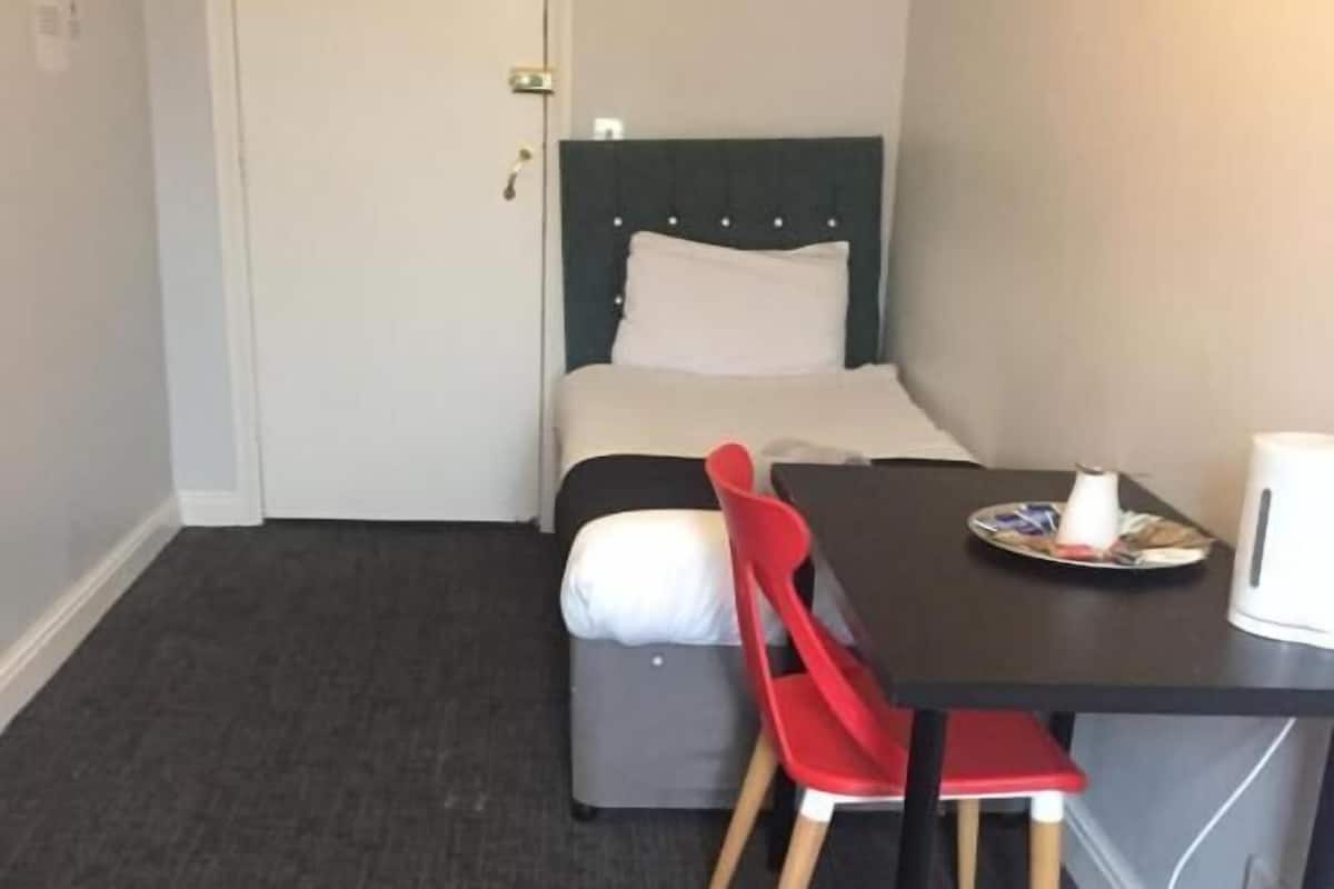 A small, compact room with a bed, a table, and a chair.