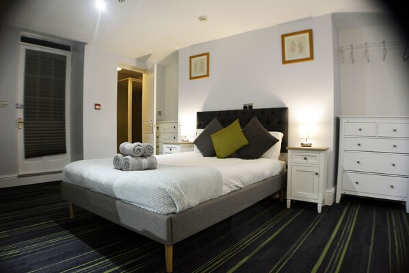 A neatly arranged bedroom with a bed, bedside tables, a dresser, and a door. - Queens Guesthouse Manchester (Manchester)