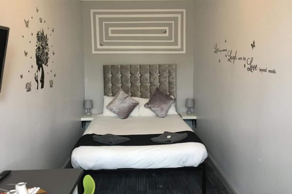 A modern bedroom with a tufted headboard, a bed with white and black bedding, two bedside lamps, and decorative wall stickers.