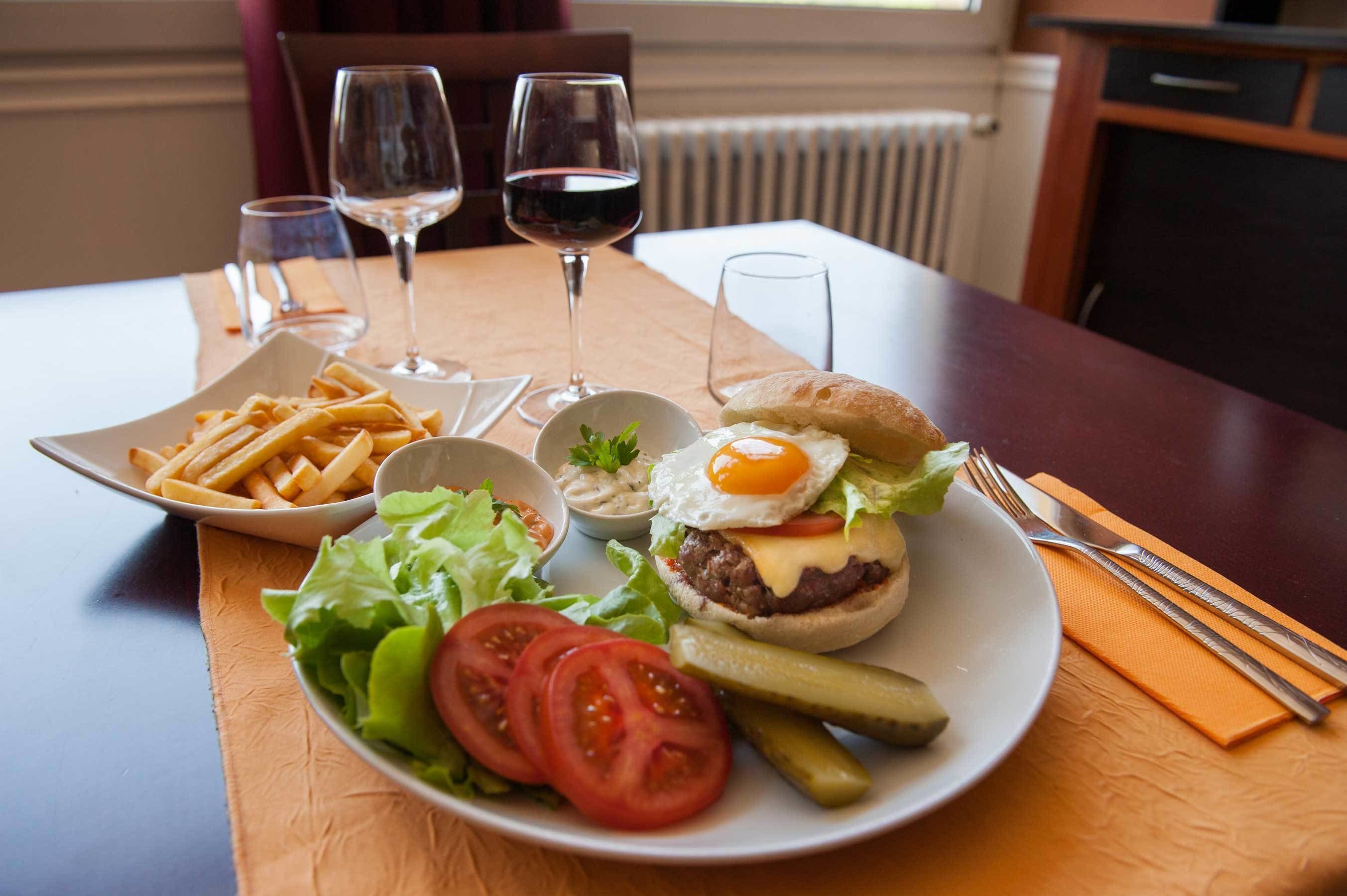 A plate with a burger, fries, and a salad on a table with two wine glasses.