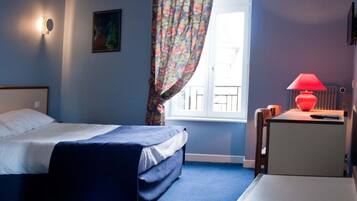 A bedroom with a bed, a desk with a lamp, a chair, a window with curtains, and a painting on the wall.