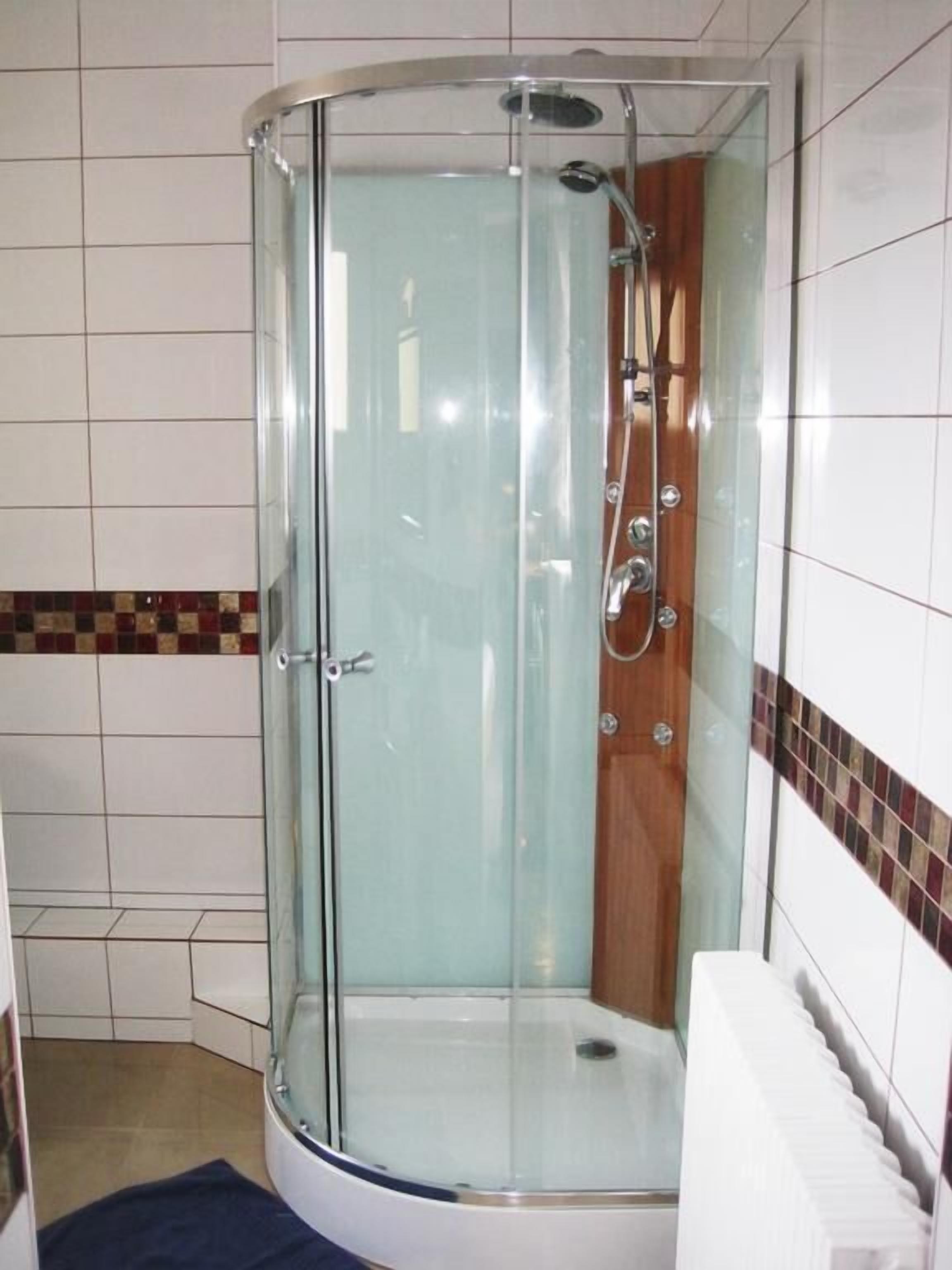 Un box de ducha con paredes de vidrio, un panel de madera y una toalla blanca colgada en la pared.