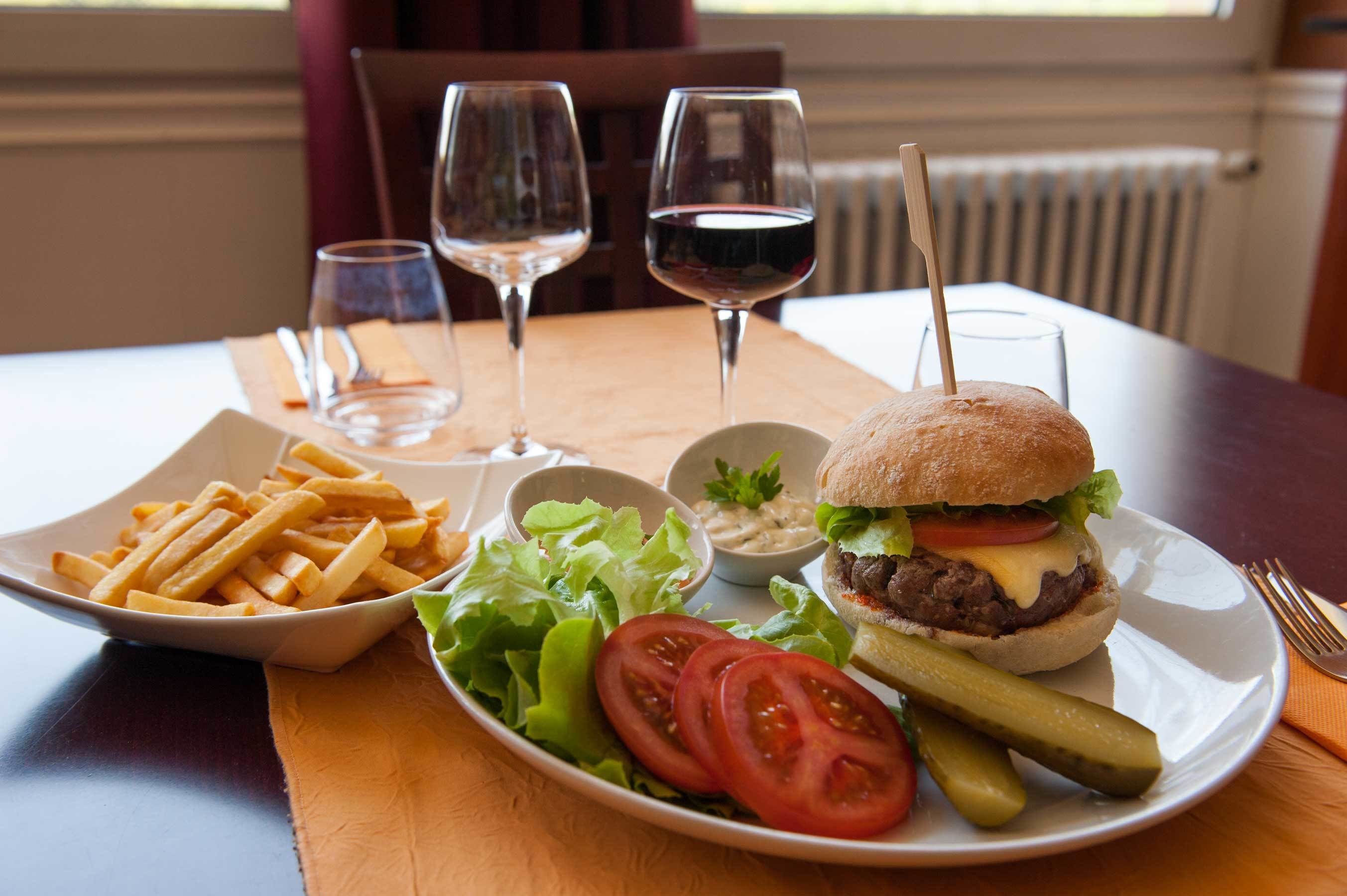 Een maaltijd bestaande uit een hamburger, frietjes, salade en een glas rode wijn op een tafel.