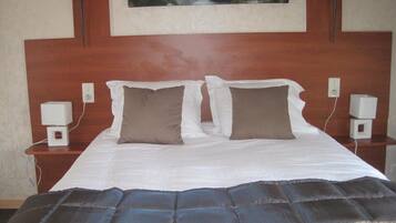 Una cama bien hecha con un colcha azul oscuro, dos almohadas blancas y un cabecero de madera.