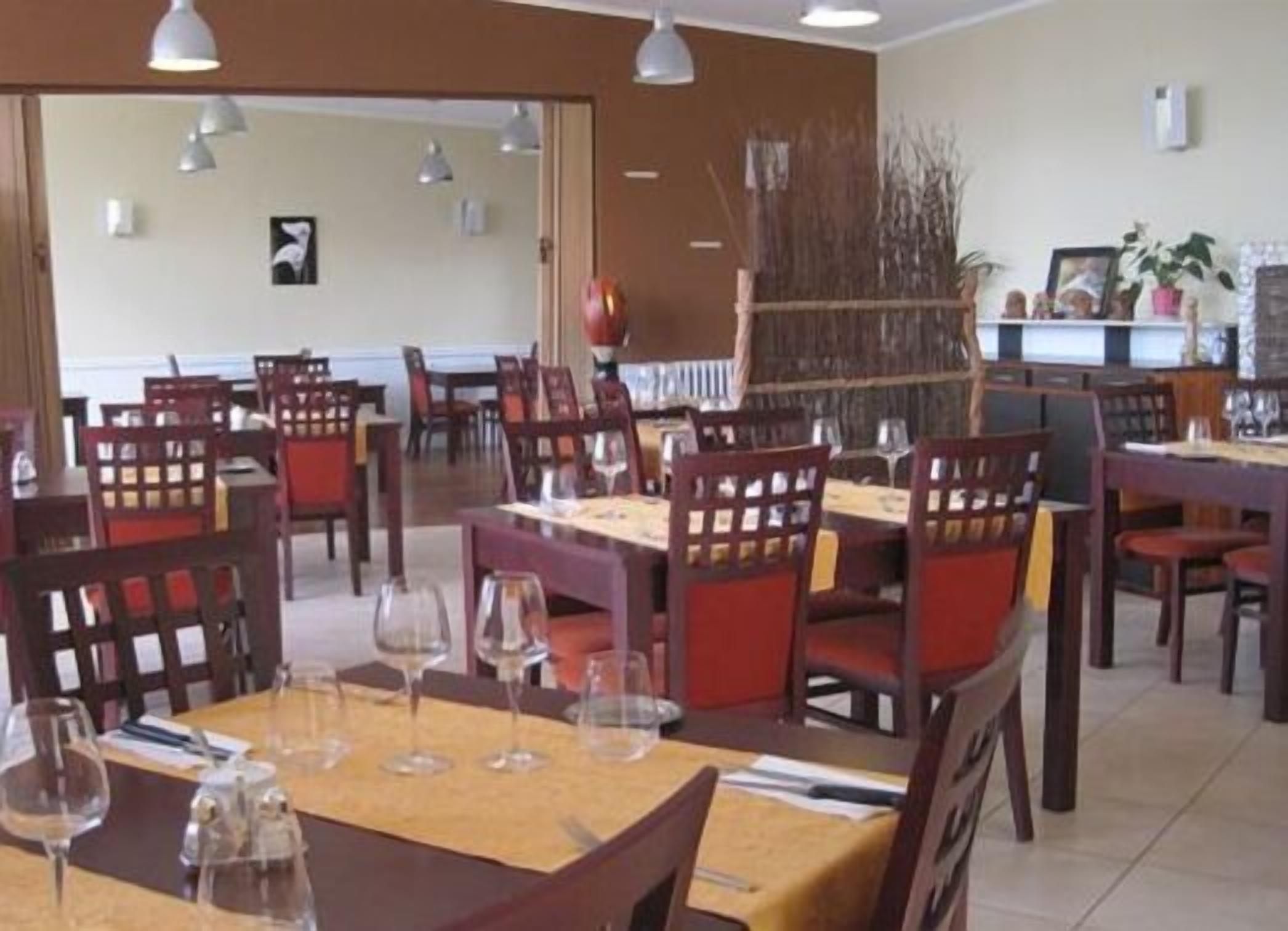 Een restaurant met meerdere tafels en stoelen, waarvan sommigen met wijnglazen.