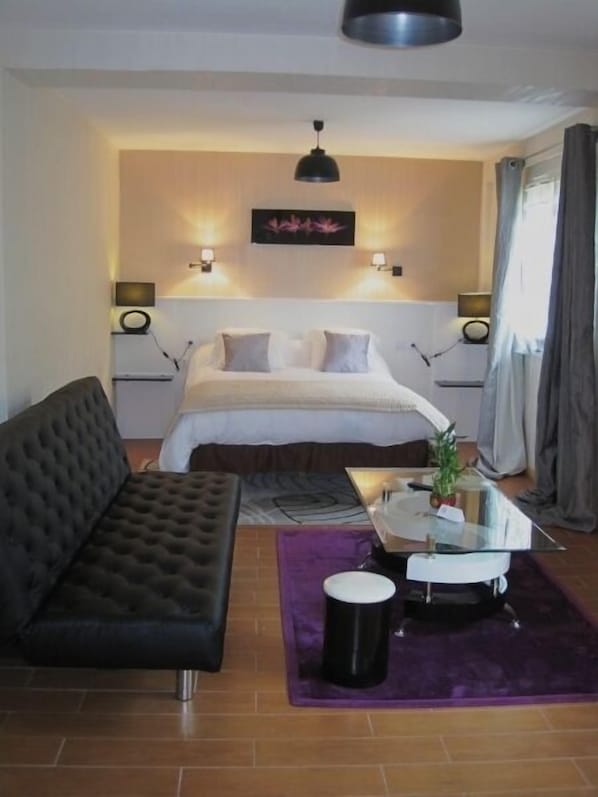 Un dormitorio moderno con cama, sofá, mesa de centro e iluminación colgante.