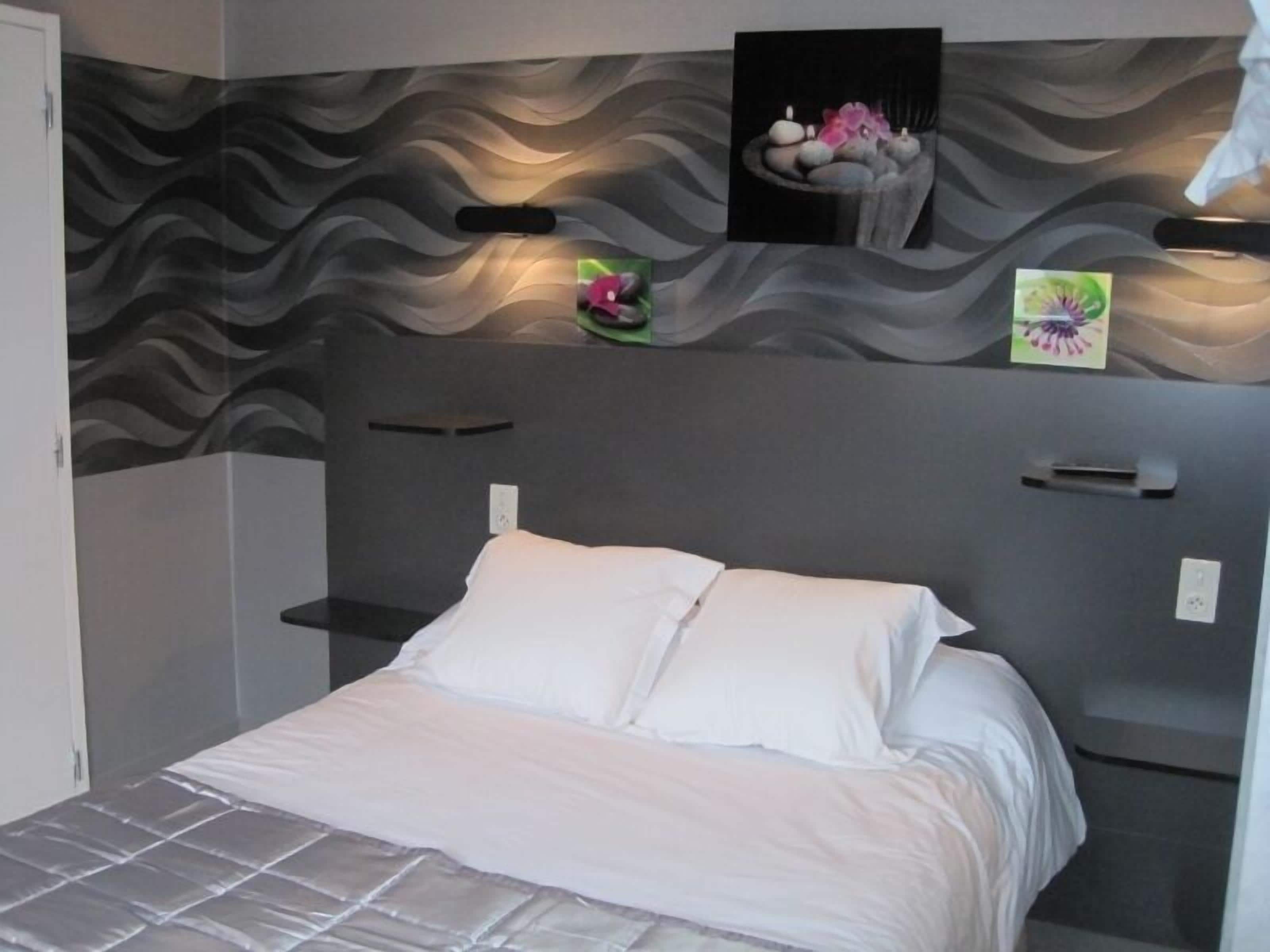 A modern bedroom with a wave-patterned headboard, a bed with white linens, and artwork on the headboard.