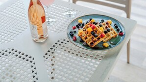 A table with a bottle of wine, two glasses of pink wine, and a plate of waffles with fruit. - Hotel Isla Bonita (San Andrés)
