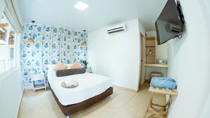 A bedroom with a bed, a TV mounted on the wall, an air conditioner, and a small table with towels. - Hotel Isla Bonita (San Andrés)