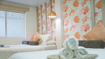 Une chambre d’hôtel avec deux lits, un papier peint à motifs floraux, un luminaire suspendu et des serviettes disposées sur le lit.