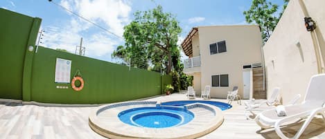 A swimming pool with lounge chairs and a lifebuoy on a green wall.