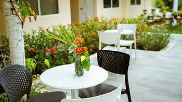 A round table with a vase of flowers, two chairs, and a white building in the background.