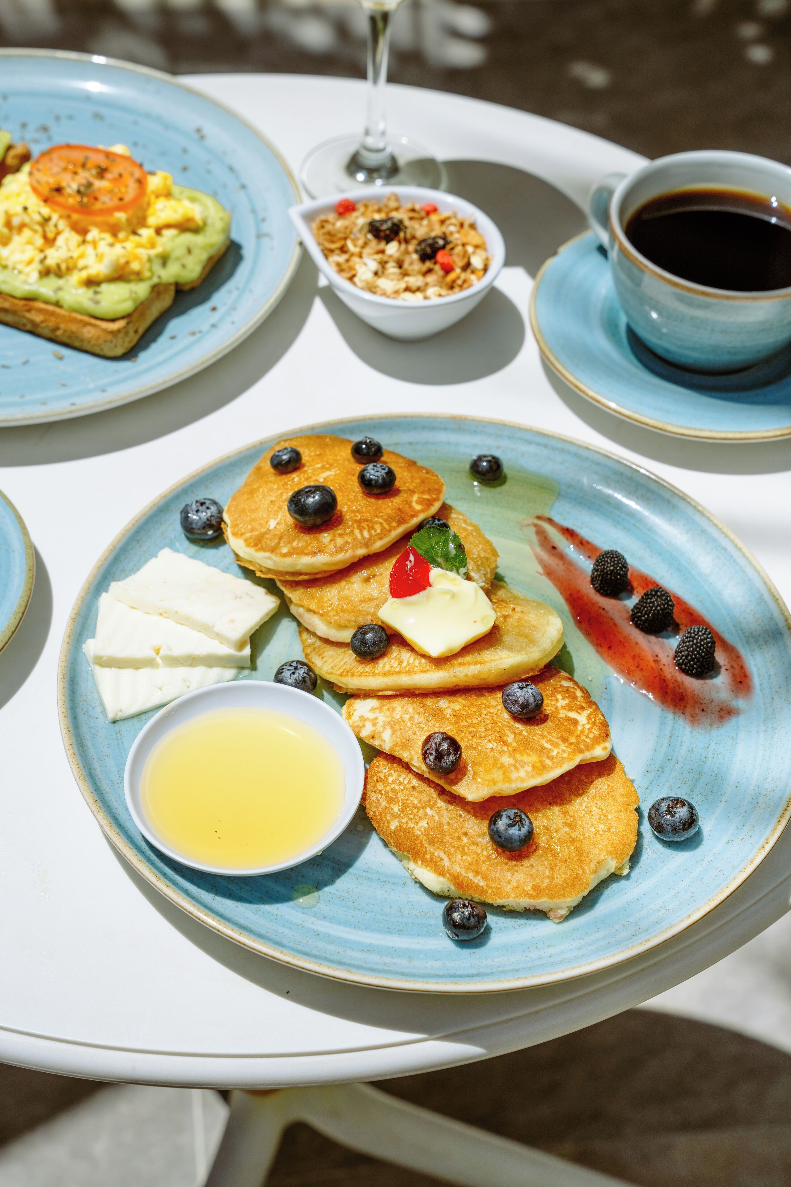 Desayuno con tortitas, arándanos y una taza de café sobre una mesa.