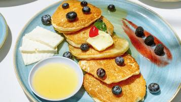 Desayuno con tortitas, arándanos y una taza de café sobre una mesa.