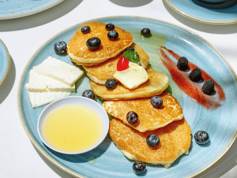 Desayuno con tortitas, arándanos y una taza de café sobre una mesa.