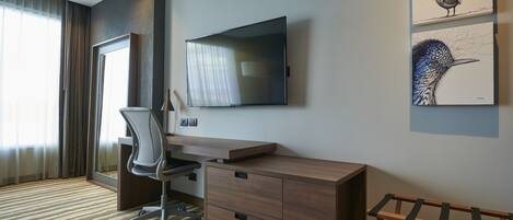 Una habitación de hotel moderna con escritorio, silla, televisor, obras de arte y ventana con cortinas.