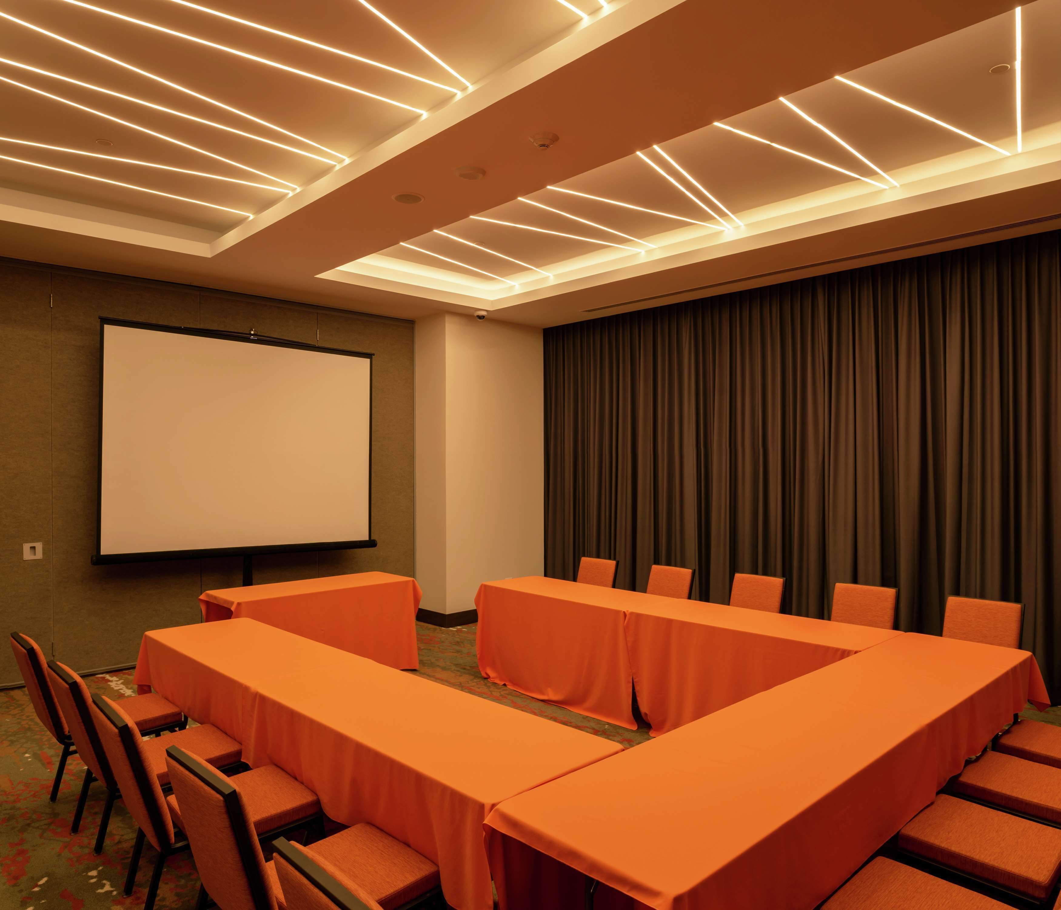A conference room with a large screen, multiple tables, and chairs.
