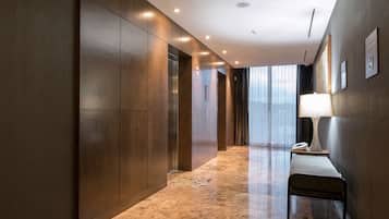 Un pasillo moderno de hotel con paneles de madera, suelo de mármol, un banco y una lámpara.