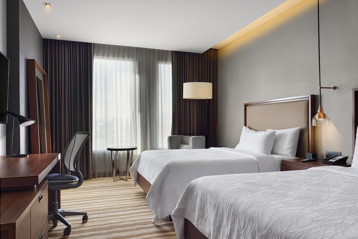 Habitación de hotel con dos camas, un escritorio, una silla, una lámpara y una mesita de noche.