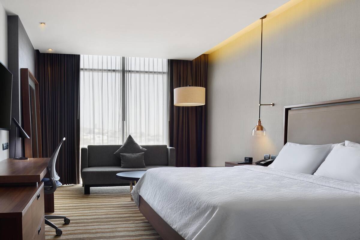 Una habitación de hotel moderna con una cama grande, un escritorio, un sofá y un televisor.