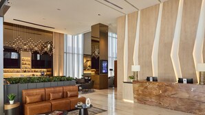 A modern lobby with a leather sofa, a reception desk, a bar area, and a large chandelier. - Hilton Garden Inn Chihuahua (Chihuahua)