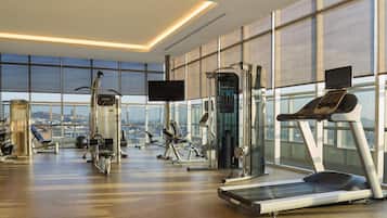 A modern gym with various exercise equipment, large windows, and a city view.
