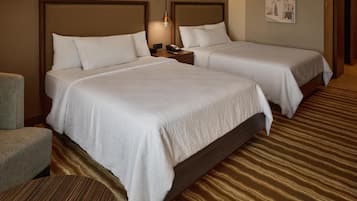 A hotel room with two beds, a nightstand with a lamp, a chair, and a patterned carpet.