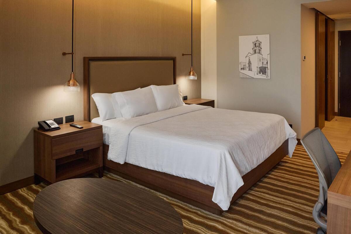 Una habitación de hotel con una cama grande, mesitas de noche, un escritorio y una silla.