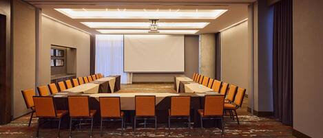 A conference room with a long table, chairs, a projector screen, and a carpeted floor.