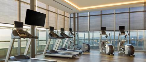 A gym with treadmills, elliptical machines, and a TV screen.