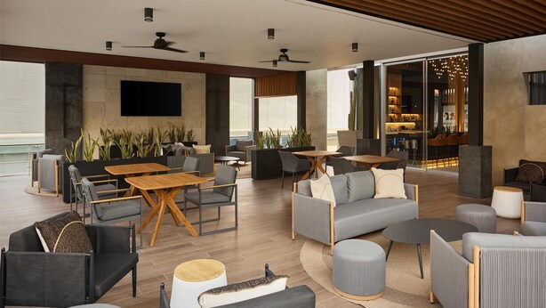 A spacious outdoor lounge area with modern furniture, a flat-screen TV, and a bar area visible through glass doors. - Hilton Garden Inn Chihuahua (Chihuahua)