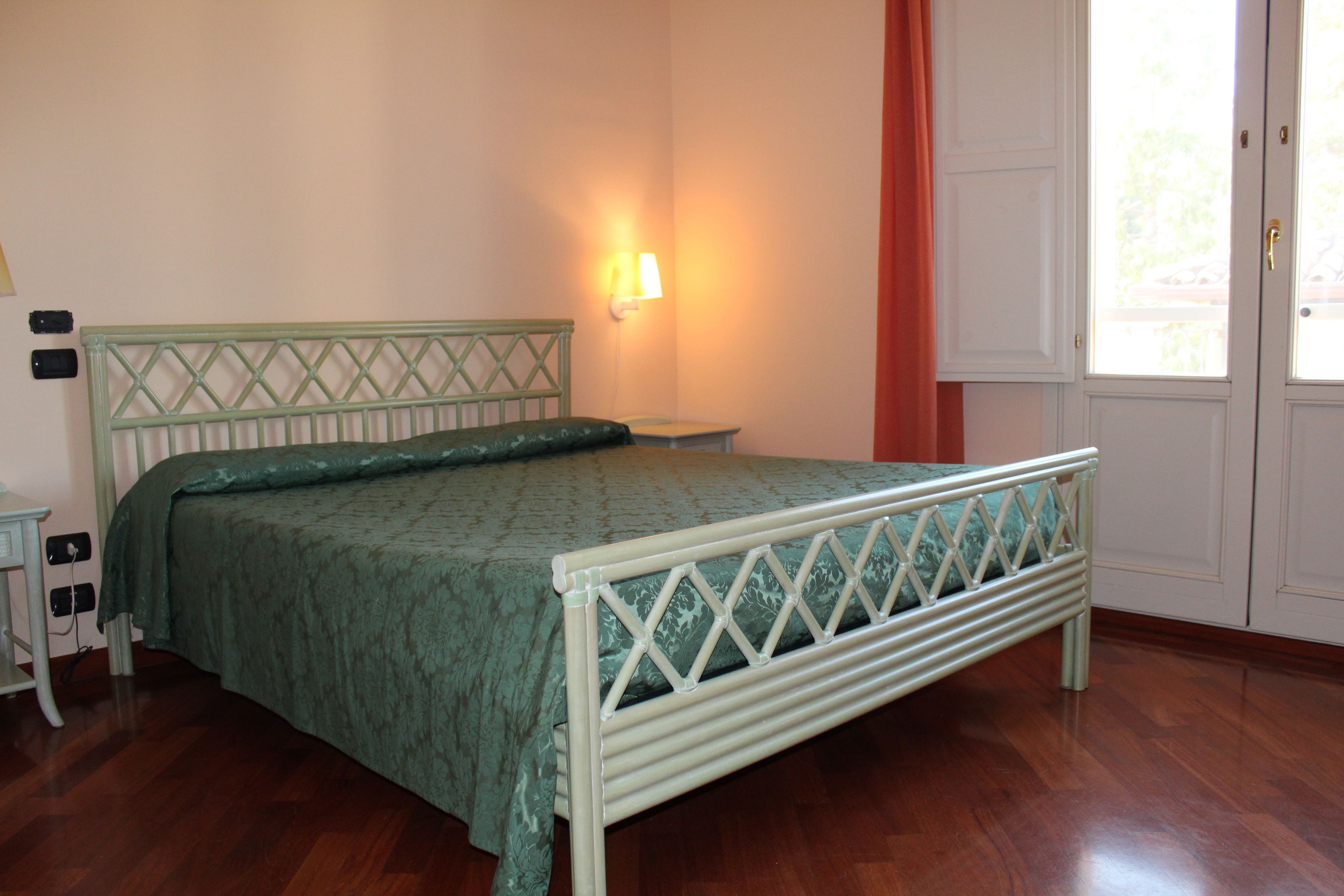 Un dormitorio con cama, mesita de noche, lámpara de pared y puerta con vistas.