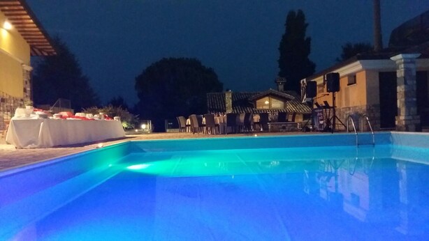 Una piscina iluminada con luz azul por la noche, rodeada de mobiliario exterior y una zona cubierta.