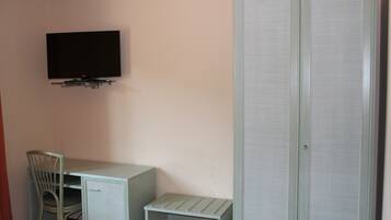 Ein Zimmer mit Schreibtisch, Stuhl, Wandfernseher und Kleiderschrank.