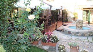 Un patio con mobiliario exterior, una fuente de piedra y plantas en macetas.