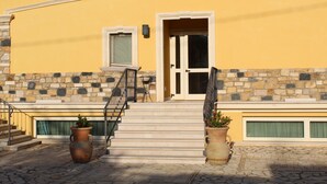 Un edificio amarillo con fachada de piedra, un conjunto de escaleras que conducen a una puerta y dos jarrones grandes con flores.