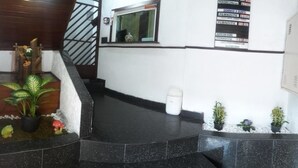 A reception area with a staircase, potted plants, and a white trash bin. - Hotel Flor da Vila Mariana (São Paulo)