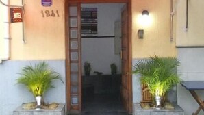 A hotel entrance with a red awning, a wooden door, and two potted plants on either side. - Hotel Flor da Vila Mariana (São Paulo)
