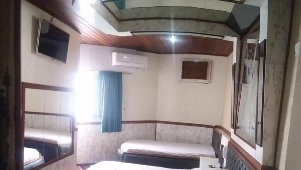A small, compact room with a bed, a bench, and a TV mounted on the wall. - Hotel Flor da Vila Mariana (São Paulo)
