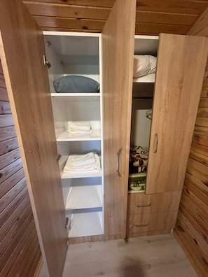 En garderob i trÀ med flera hyllor och plats för att hÀnga klÀder, en liten spegel och en dörr med ett handtag.