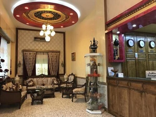 Un vestíbulo con una araña, una recepción y un área de descanso con un sofá y sillones.